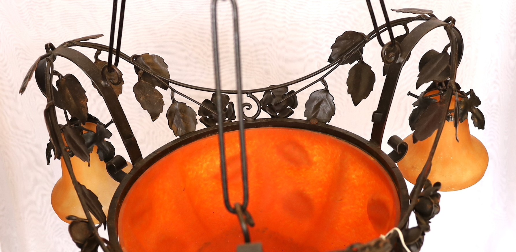 A 1930s French wrought iron and orange marbled glass light fitting decorated with rose motifs, height 97cm. width 57cm